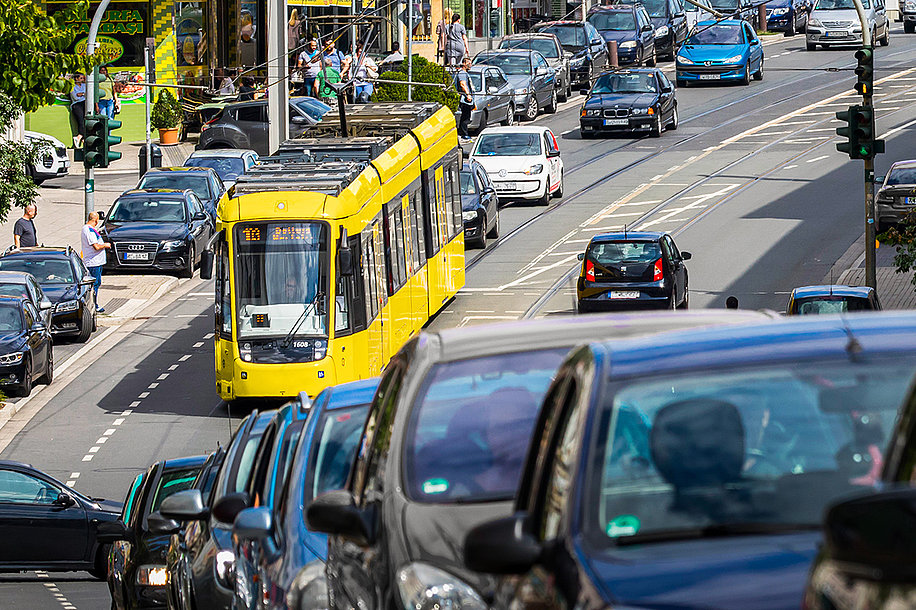 Bild einer gelben Straßenbahn mit der Linienbezeichnung 103, die eine Straße in der Stadt hochfährt. Davor und dahinter sind Autos zu sehen, die ebenfalls auf der Straße fahren.