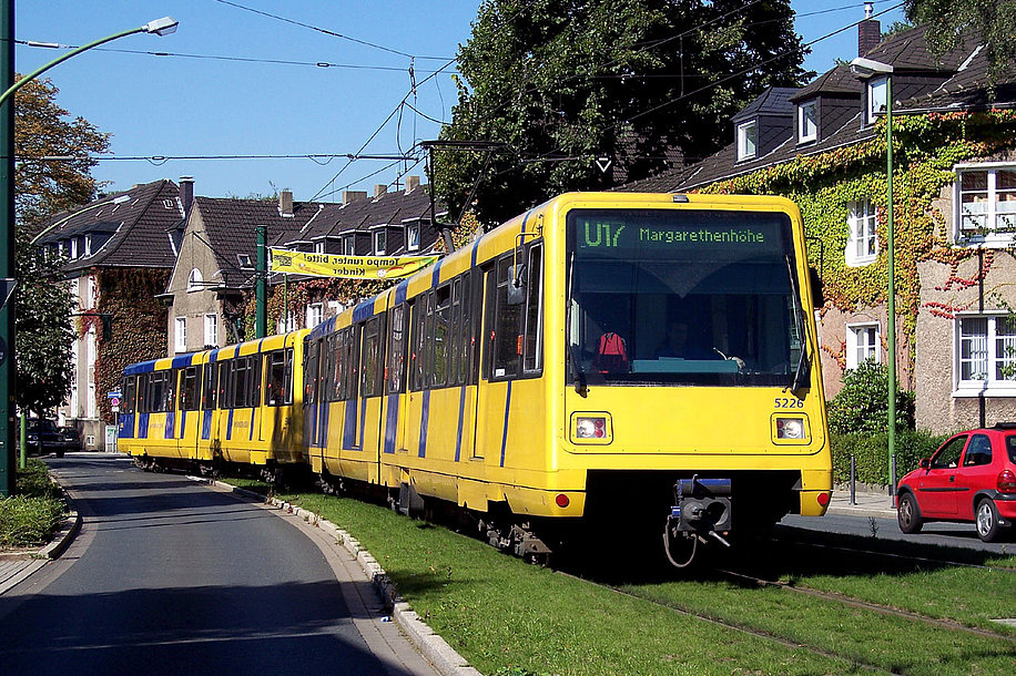 Eine gelbe Straßenbahn der Linie U17 fährt in Essen über ein Rasengleis in der Mitte einer Straße.
